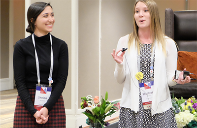 Image of two women dressed in professional attire presenting during at a conference  session.